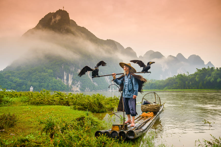 Pescador del comoran sobre una lancha enel rio yulong en yangshuo con motanas de fondo